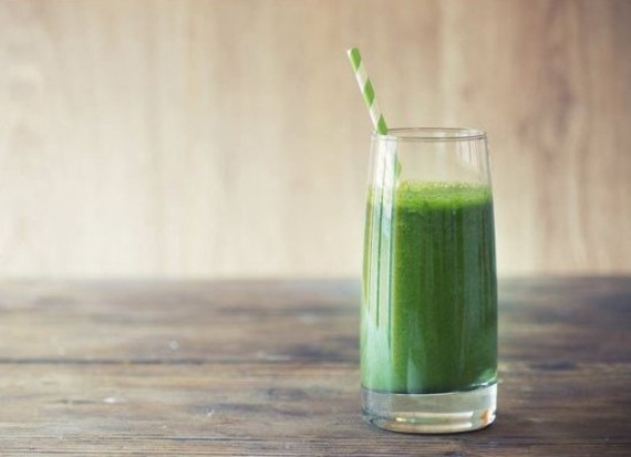 Classic green monster energy pre-workout smoothie with green and white striped straw. Sitting on a wooden table.